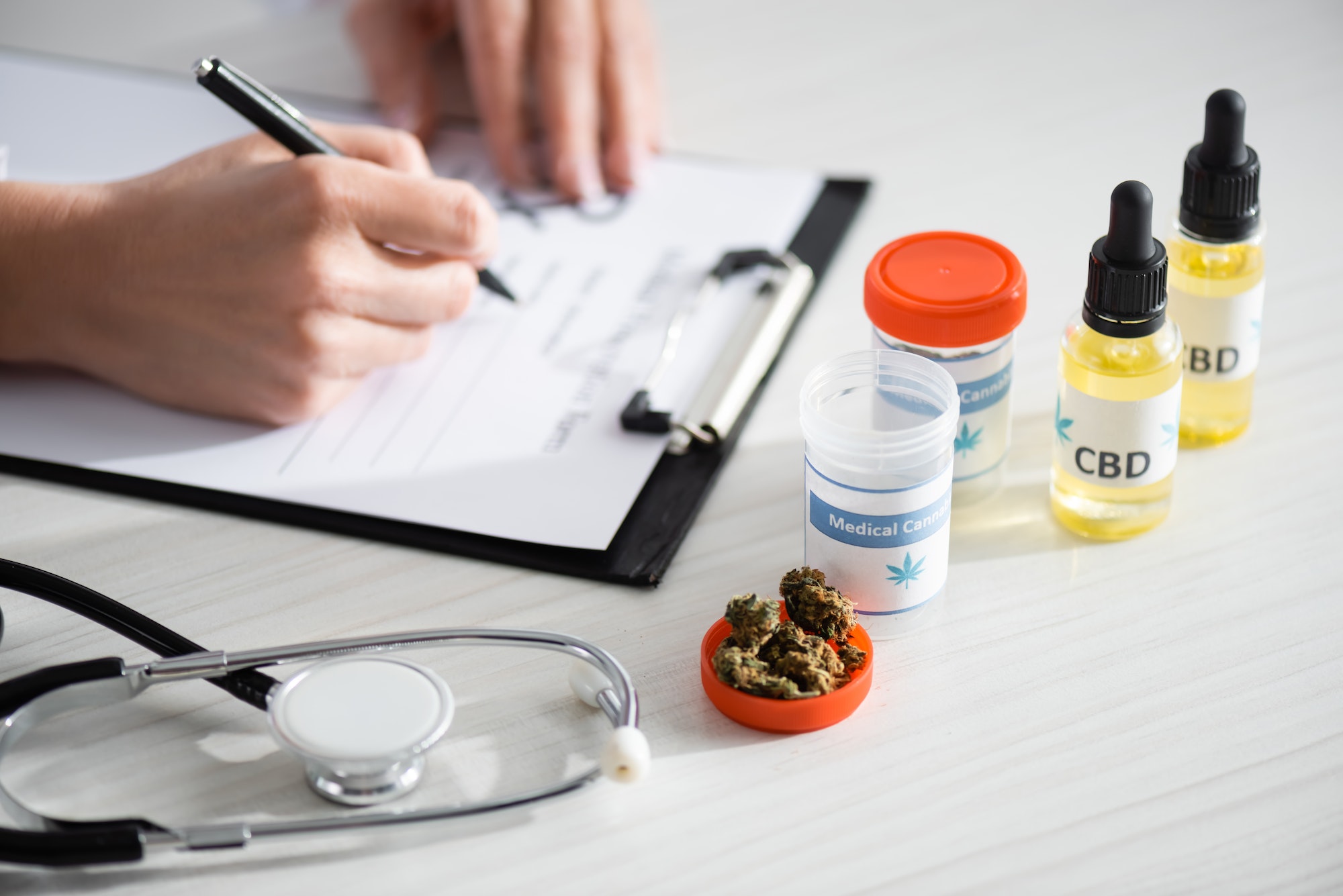 cropped view of doctor writing prescription near dried weed, bottles with cbd and medical cannabis